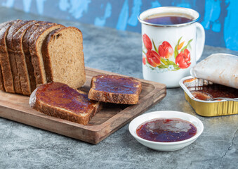 Strawberry jam with slice of brown bread and cup of tea