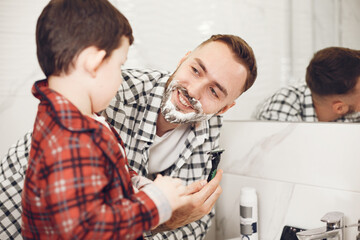 Obraz premium Father teaching his son to shave isolated. People with shaving foam in the bathroom.