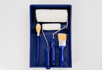 paint rollers and brushes in a blue special bath or ditch on a white background. tools for painting and repair work.