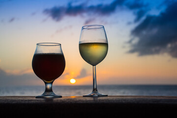 Sunset drinks. A glass of white wine and a glass of dark been are to be enjoyed by the ocean at the end of the day