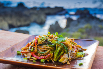 A healthy vegetable Pad Thai served on a wooden plate. This vegan dish is to be eaten in natural surroundings