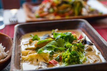vegan cuisine with drinks on a table set for two. These healthy options are Thai Green Curry with white rice and Pad Thai. Glasses of white wine and beer are also on the candlelit table
