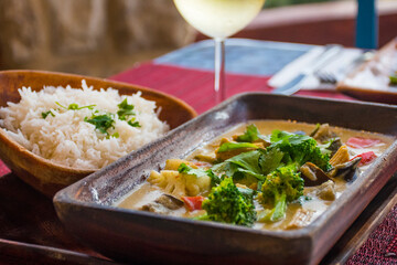vegan cuisine with drinks on a table set for two. These healthy options are Thai Green Curry with white rice and Pad Thai. Glasses of white wine and beer are also on the candlelit table