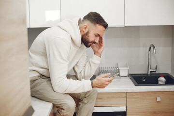 Fototapeta premium Portrait of mature man relaxin in a kitchen. Guy uses a phone.