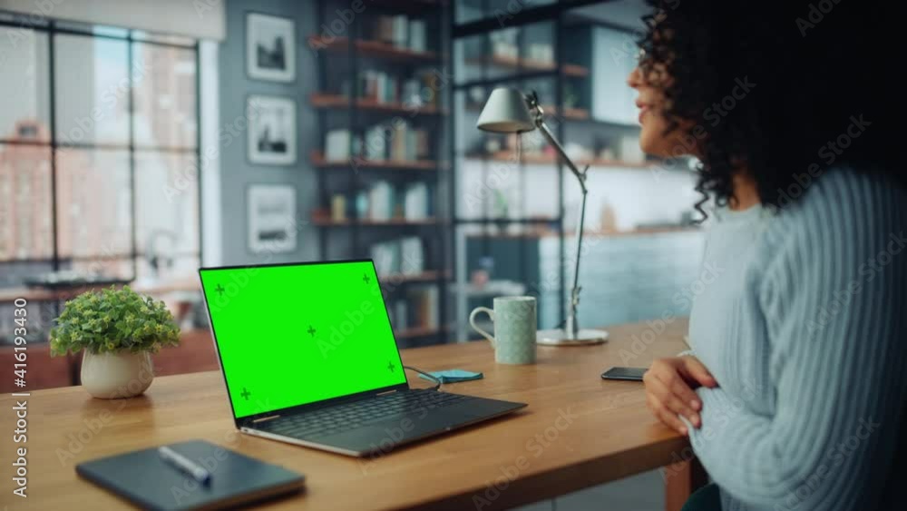 Poster close up female specialist making a video call on laptop with green screen mock up display at home l