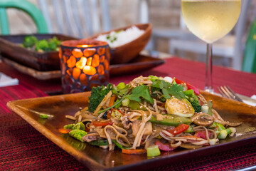 Healthy vegan Pad Thai served on a wooden plate in a relaxed environment. The meal is accompanied...