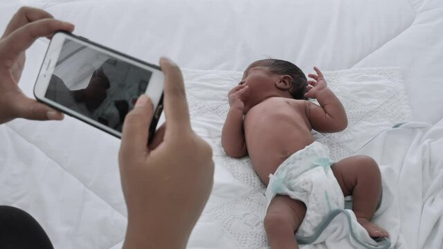 Mother take a video newborn baby into the social media for the brothers and sisters to see with Camera phone. Mixed race black boy Ethnicity Thai-Nigeria. New generation Technology Communication