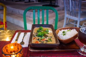 vegan cuisine with drinks on a table set for two. These healthy options are Thai Green Curry with white rice and Pad Thai. Glasses of white wine and beer are also on the candlelit table