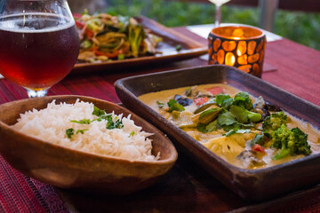 vegan cuisine with drinks on a table set for two. These healthy options are Thai Green Curry with white rice and Pad Thai. Glasses of white wine and beer are also on the candlelit table