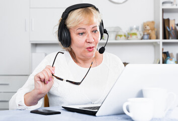 Happy mature woman in headphones with microphone communicating via internet