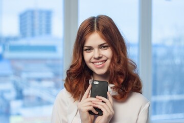 cheerful red-haired woman with a phone in her hands communicating an official office