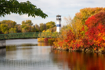 Fototapeta na wymiar Beautiful autumn scene of a lighthouse on the river shore with trees turning red, yellow, and orange
