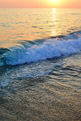 Sunset on sea beach, waves and surf with white foam on wet sand. Vertical frame