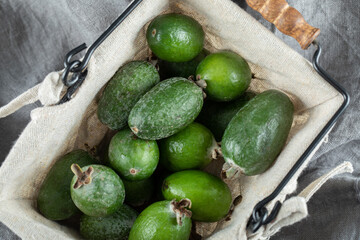 A basket full of feijoa on a gray tablecloth