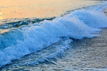Fototapeta premium Sunset on sea beach, waves and surf with white foam on wet sand. Horizontal frame