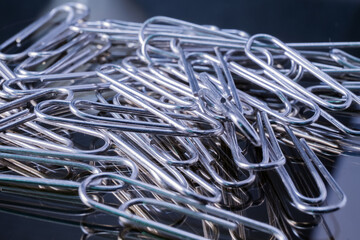 many metal paper clip on black mirror with lighting from above 