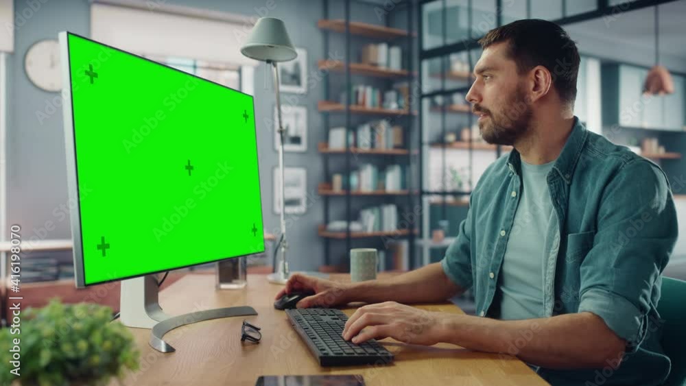Poster handsome caucasian specialist working on desktop computer with green screen mock up display at home 