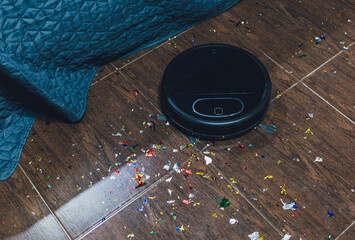 Modern black robotic vacuum cleaner removing litter from brown wooden floor. Cleaning at home, top...