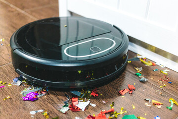 Modern black robotic vacuum cleaner removing litter from brown wooden floor. Cleaning at home, top...