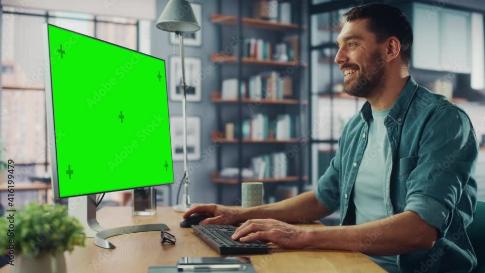 Poster handsome caucasian specialist working on desktop computer with green screen mock up display at home 