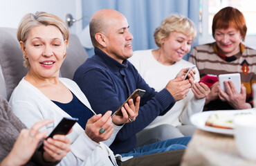 Obraz premium Mature friends are resting together and looking at their phones at home.