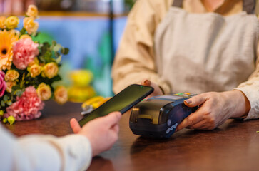 Close-up of a shopper's hands with a phone making contactless payments using nfc technology at the cashier terminal in a flower shop