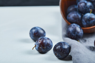 Ripe plums in a bowl with gray tablecloth on white table