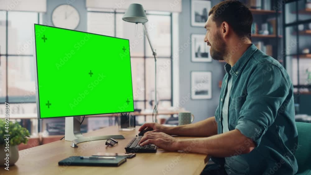 Poster handsome caucasian specialist working on desktop computer with green screen mock up display at home 
