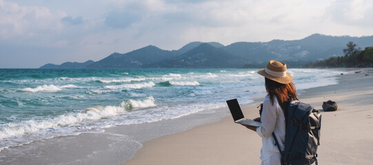 A female traveler using and working on laptop computer while walking on the beach