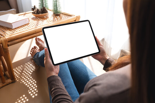 Mockup image of a woman holding and using tablet pc with blank desktop white screen at home