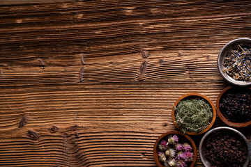 Natural medicine background. Assorted dry herbs in bowls and brass mortar on rustic wooden table.