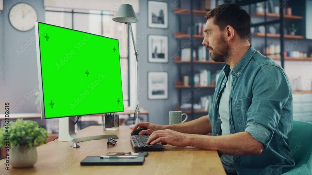 Poster handsome caucasian specialist working on desktop computer with green screen mock up display at home 