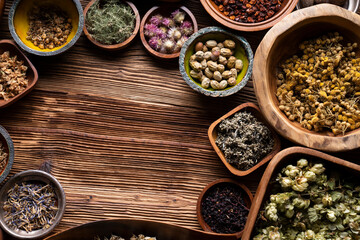 Natural medicine background. Assorted dry herbs in bowls and brass mortar on rustic wooden table.