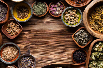 Natural medicine background. Assorted dry herbs in bowls and brass mortar on rustic wooden table.