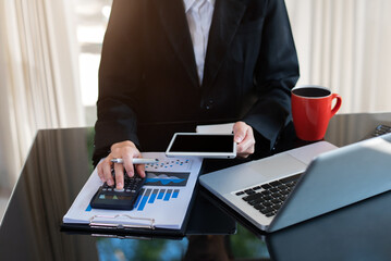 Businesswoman working with tablet and using a calculator to calculate the numbers of static in...