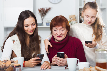 Three generations of women of one modern family absorbedly looking at phones