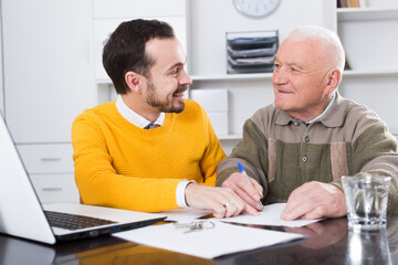 Old male client signing agreement papers in office with manager