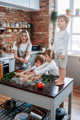 Domestic kitchen of casual family in modern apartment. Group of three little brother learn to cook with their mother.
