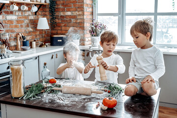 Warm portrait of good relationship of brothers. Three preschool kids have a good time and learning cooking in modern kitchen.
