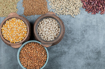 Different kinds of bean seeds, lentil, peas in dishes on a dark background