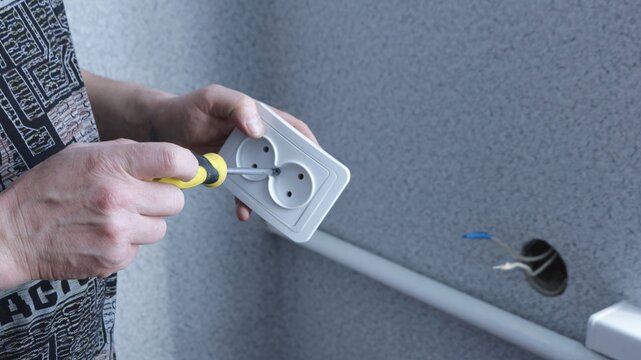 screwing the bolt into the corus of the cutter that the man holds in his hands before installing and connecting with the electric wires in the round hole of the cutter, men's homework with tools