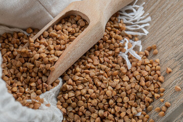 A wooden spoon full of raw buckwheat on a wooden table