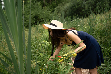 a girl of Asian appearance, in a straw hat and dress, is looking for something in the bushes