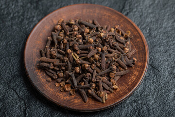 A brown plate full of dried cloves on a dark background
