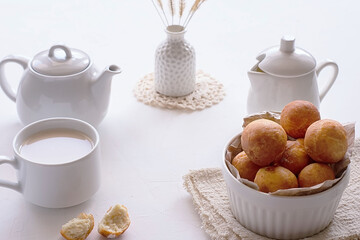 White teapot, a cup of tea and a bowl with donuts on a light background. Breakfast concept