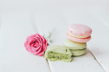 On a wooden background there are two macarons, one green and the other pink, and a beautiful rose with a half macaroon in front of a white background