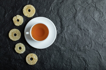 A cup of aroma tea with dried pineapple on a dark background