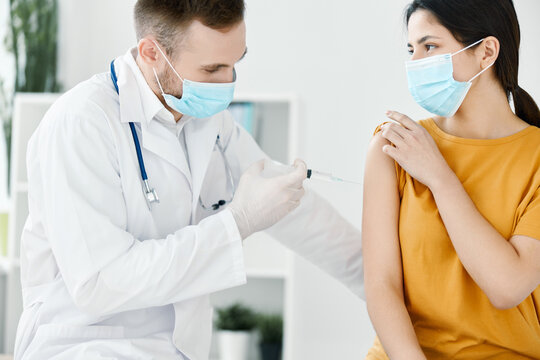doctor's assistant injections in the shoulder of a woman wearing a medical mask covid vaccination