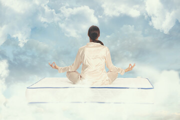 Young woman meditating on mattress soft as clouds in blue sky