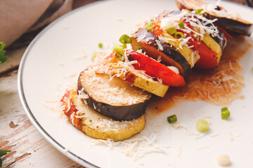 Plate of tasty baked eggplant and tomatoes on light wooden background